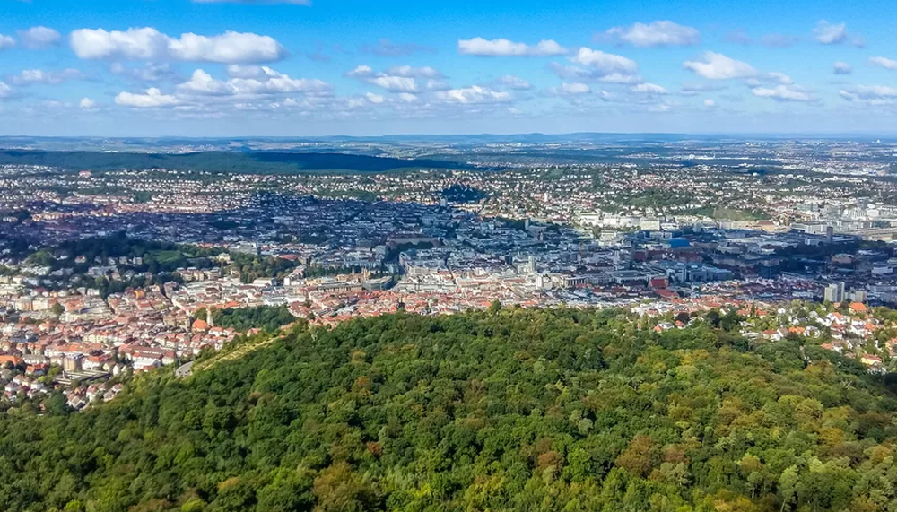 Blick über eine Stadt, im Vordergrund ist viel Wald zu sehen.